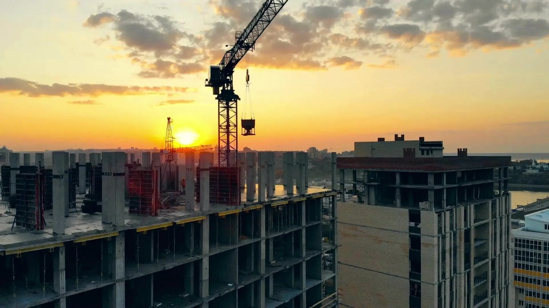 Reinforced-concrete construction rising at sunset with a tower crane