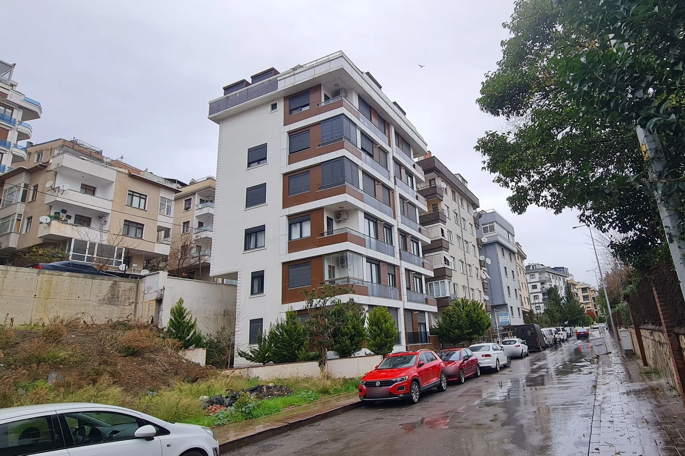 Örtülü Apartments in İdealtepe: a modern residential building with warm wood-toned balcony bands and a white volume on a tree-lined street