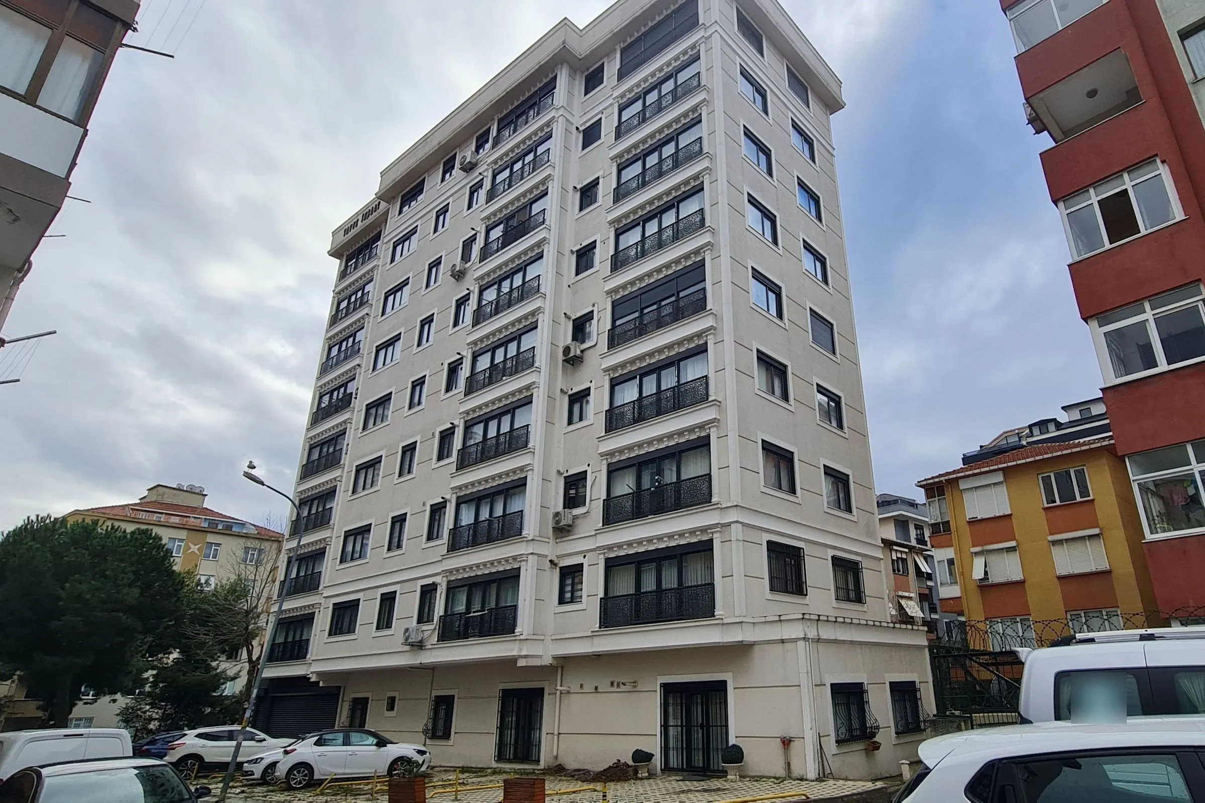 Bağlarbaşı’nda Yıldız Apartmanı: her katta klasik korniş profilleri ve siyah işlemeli balkon korkulukları olan yüksek krem cepheli bina