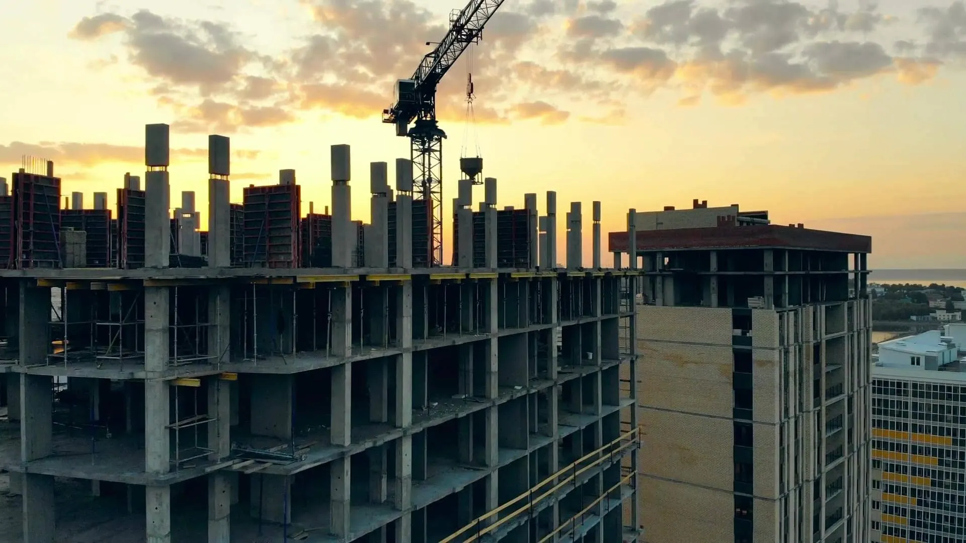 A reinforced-concrete residential building rising at sunset with a tower crane